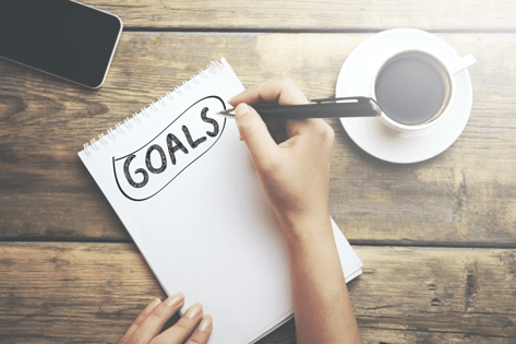 A person writing the word 'goals' at the top of a notebook page