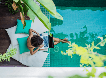 a woman sat by a pool working from a laptop