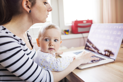 woman working on a laptop with a baby on her knee