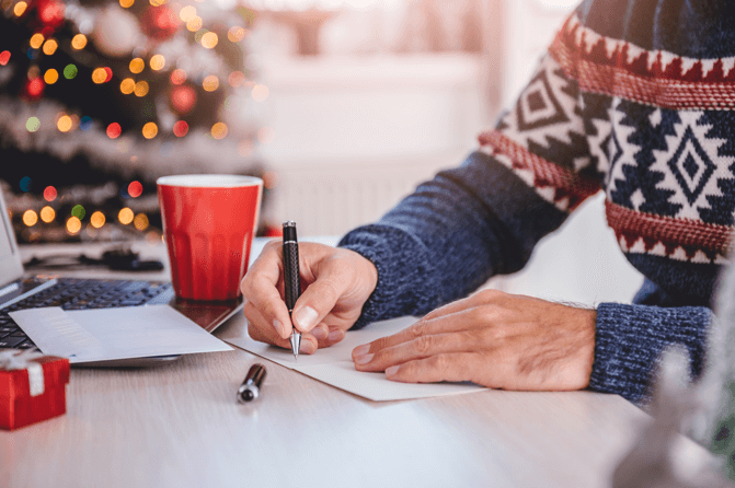 Man in a Christmas jumper writing out a card