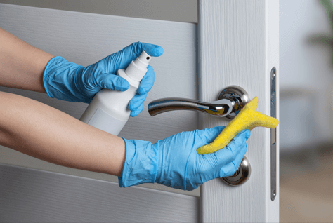 pair of hands with blue gloves cleaning a door handle