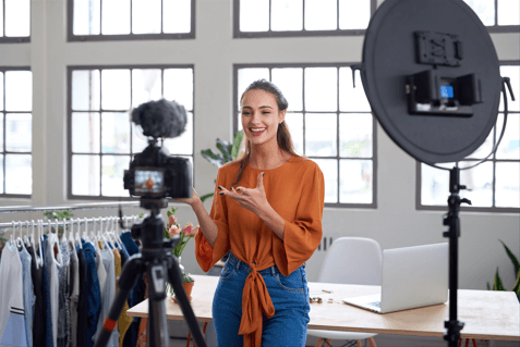 lady in an orange blouse talking to a camera about clothes