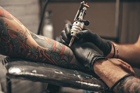 tattoo artist tattooing a sleeve of art on someone's arm