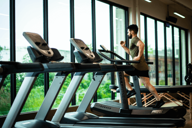 man running on a treadmill facing a window in a gym