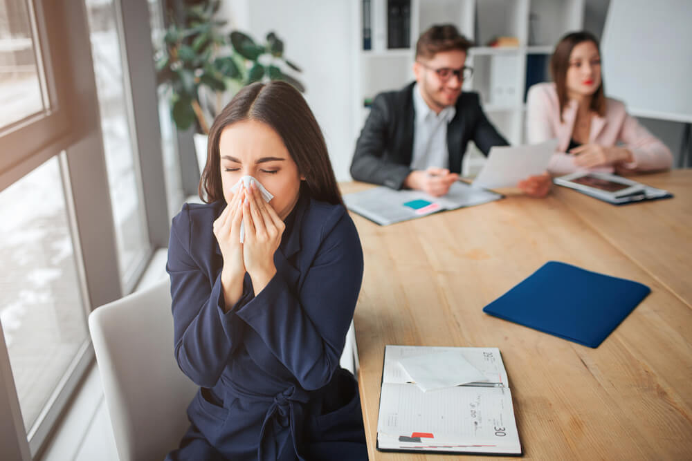 woman sneezing into a tissue in a work meeting