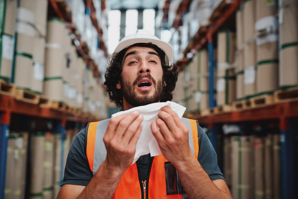 man in high vis jacket sneezing in a warehouse