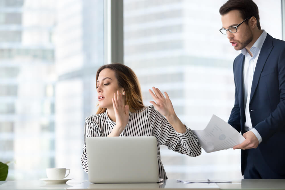 Woman holding hands up to stop man from talking at a desk